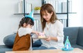 Millennial Asian young female teenager mother nanny babysitter sitting holding dish while little cute preschooler daughter Royalty Free Stock Photo