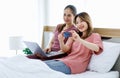 Asian young happy female  LGBTQ lover couple sitting together on bed under warm blanket holding credit Royalty Free Stock Photo