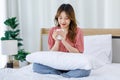 Millennial Asian young happy cheerful female teenager sitting smiling on cozy bed in bedroom at home while drinking hot coffee in Royalty Free Stock Photo