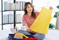 Millennial Asian young happy cheerful thoughtful female teenager sitting smiling on cozy bed in bedroom at home checking clothes Royalty Free Stock Photo