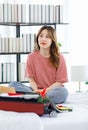 Millennial Asian young happy cheerful thoughtful female teenager sitting smiling on cozy bed in bedroom at home checking clothes Royalty Free Stock Photo