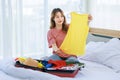 Millennial Asian young happy cheerful thoughtful female teenager sitting smiling on cozy bed in bedroom at home checking clothes Royalty Free Stock Photo