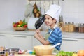 Millennial Asian young little boy chef wearing white tall cook hat and apron standing smiling holding cooking pan posing taking Royalty Free Stock Photo