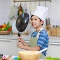 Millennial Asian young little boy chef wearing white tall cook hat and apron standing smiling holding cooking pan posing taking Royalty Free Stock Photo