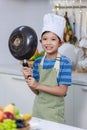 Millennial Asian young little boy chef wearing white tall cook hat and apron standing smiling holding cooking pan posing taking Royalty Free Stock Photo