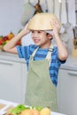 Millennial Asian young little boy chef wearing white tall cook hat and apron standing smiling holding wooden bowl on head posing Royalty Free Stock Photo