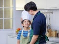 Millennial Asian young little boy pastry chef wearing white tall cook hat and apron standing smiling posing together with father Royalty Free Stock Photo