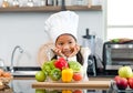 Millennial Asian young little cute girl chef daughter with white tall cook hat and apron standing smiling holding wooden spoon and Royalty Free Stock Photo