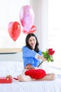 Millennial Asian young romantic cheerful female girlfriend sitting on bed in bedroom decorate with pink heart shape balloon Royalty Free Stock Photo