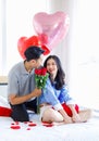 Millennial Asian young romantic lover couple male boyfriend holding red roses bouquet giving surprised to female girlfriend on bed Royalty Free Stock Photo