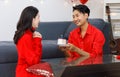 Millennial Asian young romantic lover couple male boyfriend in red outfit sitting on floor giving surprising female girlfriend