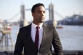 Millennial black businessman wearing black jacket, white shirt and tie standing at the Thames riverside in London, Tower Bridge in Royalty Free Stock Photo