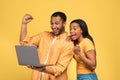 Millennial black couple making YES gesture, looking at laptop, celebrating success or achievement on yellow background Royalty Free Stock Photo