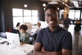 Millennial black male creative standing in a busy casual office, smiling to camera Royalty Free Stock Photo