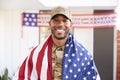 Millennial African American  soldier with US flag draped over his shoulders, smiling to camera, close up Royalty Free Stock Photo