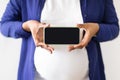 Millennial black woman in domestik clothes with big belly enjoys pregnancy, holds smartphone with empty screen Royalty Free Stock Photo