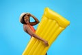 Millennial black woman in swimsuit holding yellow inflatable lilo on blue studio background Royalty Free Stock Photo