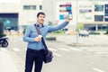 Millennial business man with hand up calling taxi or ride share car hailing from sidewalk