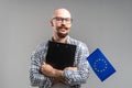 Millennial caucasian businessman holding clipboard and European Union flag. Young balded bearded guy.