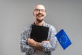 Millennial caucasian businessman holding clipboard and European Union flag. Young balded bearded guy.