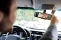 Millennial caucasian guy in suit with hands on steering wheel, configures mirror