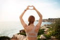 Millennial caucasian woman in sportswear doing arm exercise and heart sign, looks at ocean beach Royalty Free Stock Photo