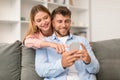 Millennial couple engrossed in smartphone browsing social media at home