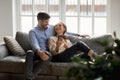 Millennial couple in love seated on couch talking using smartphone