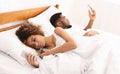 Millennial couple lying on bed back to back with smartphones Royalty Free Stock Photo