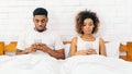 Millennial couple lying in bed separately with smartphones Royalty Free Stock Photo
