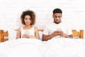 Millennial couple lying in bed separately with smartphones Royalty Free Stock Photo