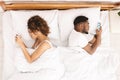 Millennial couple lying on bed back to back with smartphones Royalty Free Stock Photo