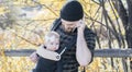 Millennial Dad with Baby in Carrier Outside Talking and Texting