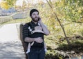 Millennial Dad with Baby in Carrier Outside Talking and Texting