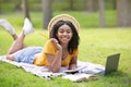 Millennial female student with laptop lying on blanket at park in summer, blank space Royalty Free Stock Photo