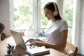 Millennial female studying working online using laptop and wireless headphones