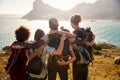 Millennial friends on a hiking trip reach the summit and embrace, admiring the view, back view Royalty Free Stock Photo