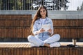 Millennial girl in denim sits on park bench holding smart tablet. Woman uses tablet to shop on Internet, sits on street. Royalty Free Stock Photo