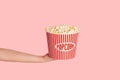 Millennial girl holding bucket of fresh crunchy popcorn over pink background, close up Royalty Free Stock Photo