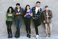 Millennial group of women and men are on their smart phones - Leaning against the wall - Casual - Smiling and Happy Royalty Free Stock Photo