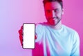 Millennial guy holds touchscreen phone in hand with blank screen in neon light