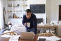 Millennial African American  man stands leaning on table in the dining room holding cup and looking down at his laptop computer sc Royalty Free Stock Photo