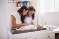 Millennial Hispanic mother and grandmother playing with baby son on changing table, selective focus Royalty Free Stock Photo