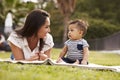 Millennial Hispanic mother lying beside her baby, sitting on a blanket in the park, close up