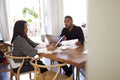 Millennial man with laptop computer giving financial advice to a woman sitting at the table holding a document in her dining room, Royalty Free Stock Photo