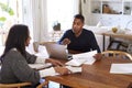 Millennial man with laptop computer giving financial advice to a woman sitting at the table holding a document in her dining room, Royalty Free Stock Photo