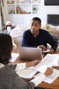 Millennial man with laptop computer giving financial advice to a woman sitting at the table holding a document in her dining room, Royalty Free Stock Photo