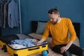 Millennial man making check-list of things to pack for travel at home. Packing suitcase at home. Travel concept