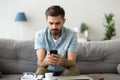 Confused man sit on couch shocked using smartphone