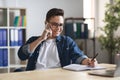 Millennial man writing notes while making phone call at workplace in office Royalty Free Stock Photo